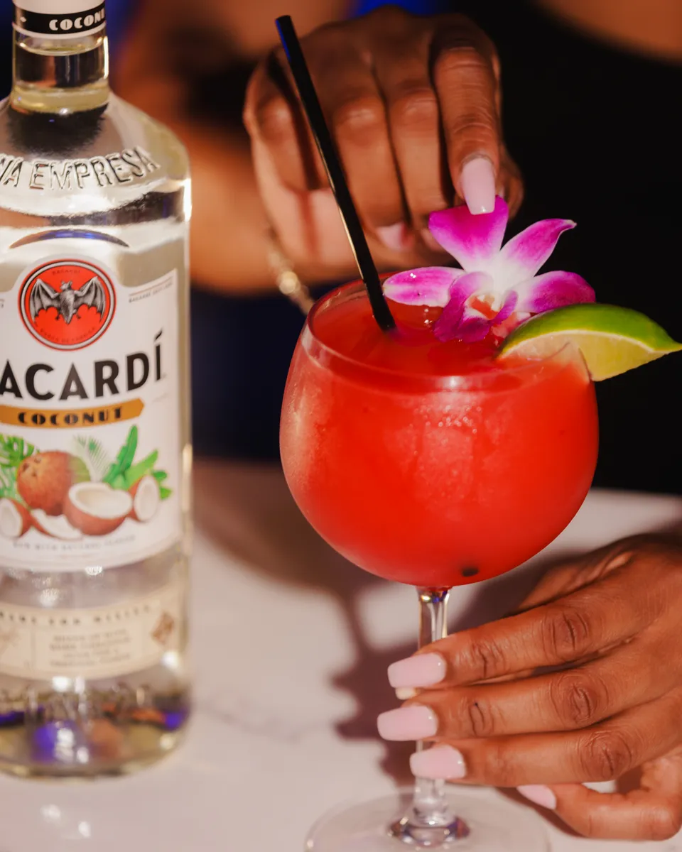 Red daiquiri with orchid garnish beside a coconut rum bottle