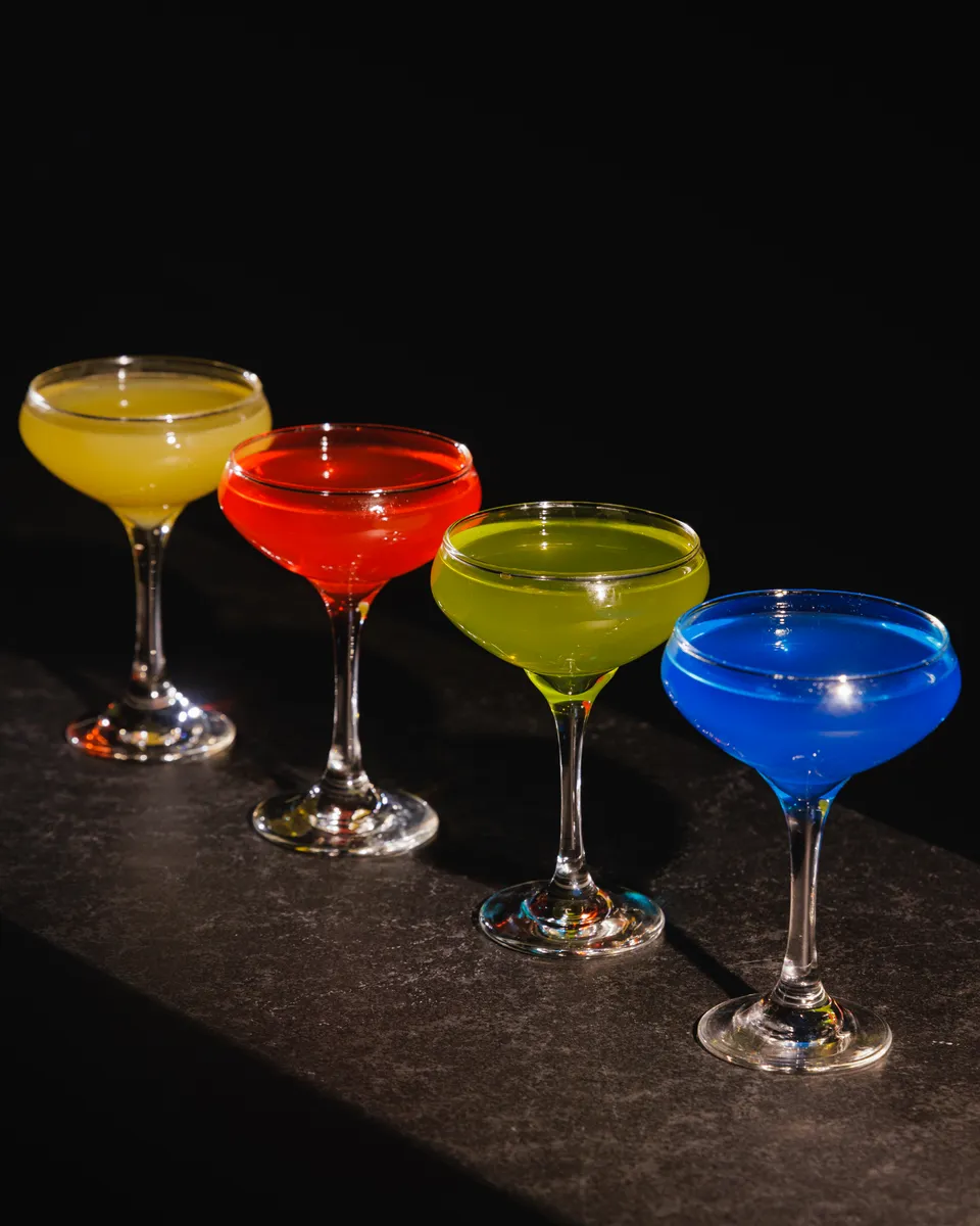 Lineup of colorful coupe cocktails in yellow, red, green, and blue