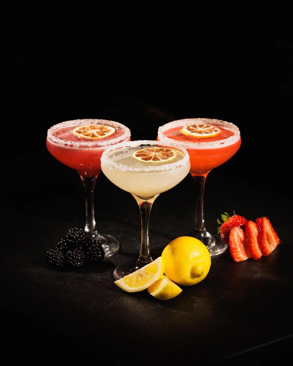 Trio of craft coupe cocktails with dried citrus, lemon, and strawberries