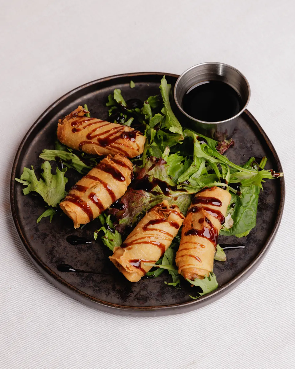 Crispy rolls drizzled with sauce over greens on a slate plate
