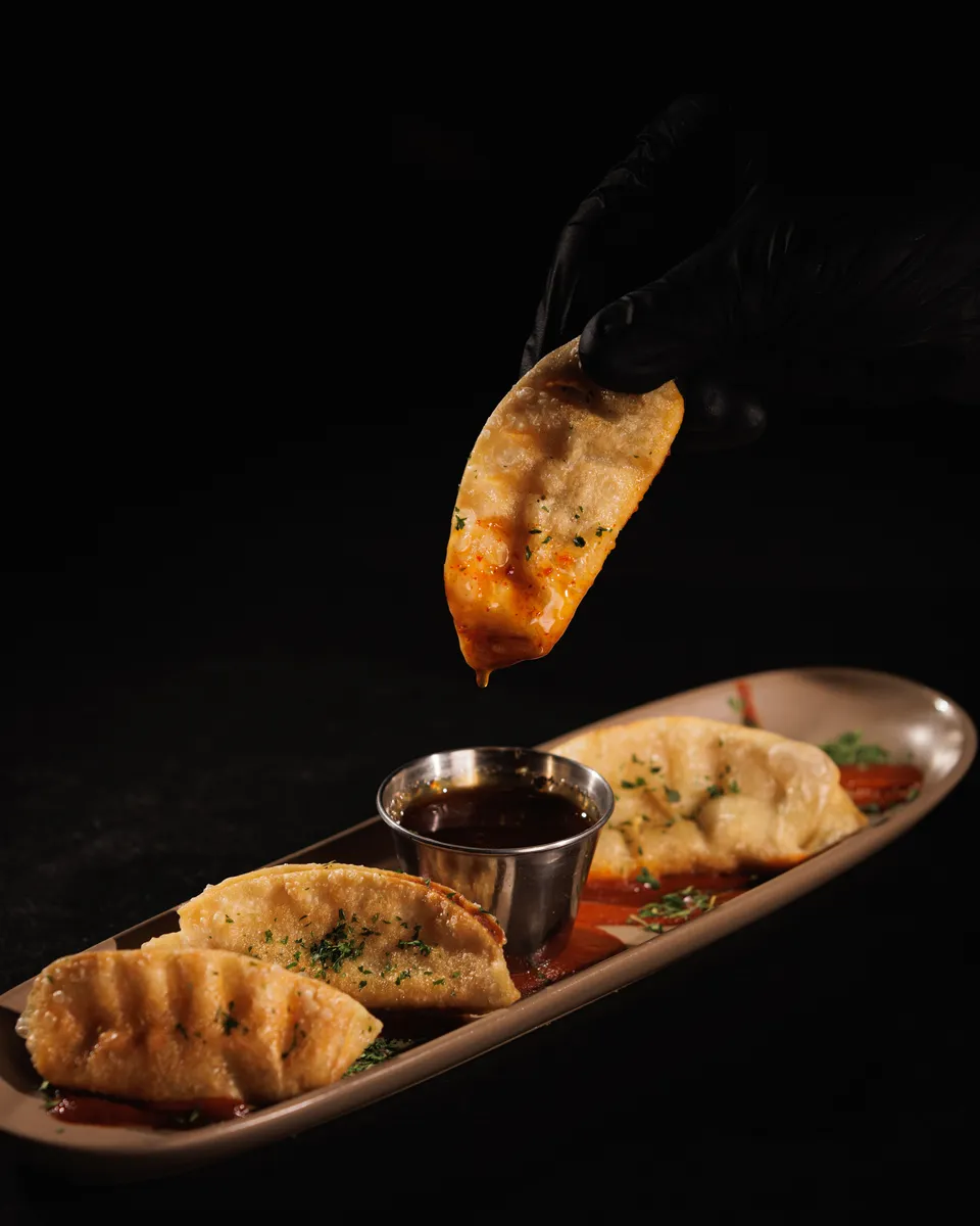 Pan-fried dumplings with dipping sauce, one held mid-air