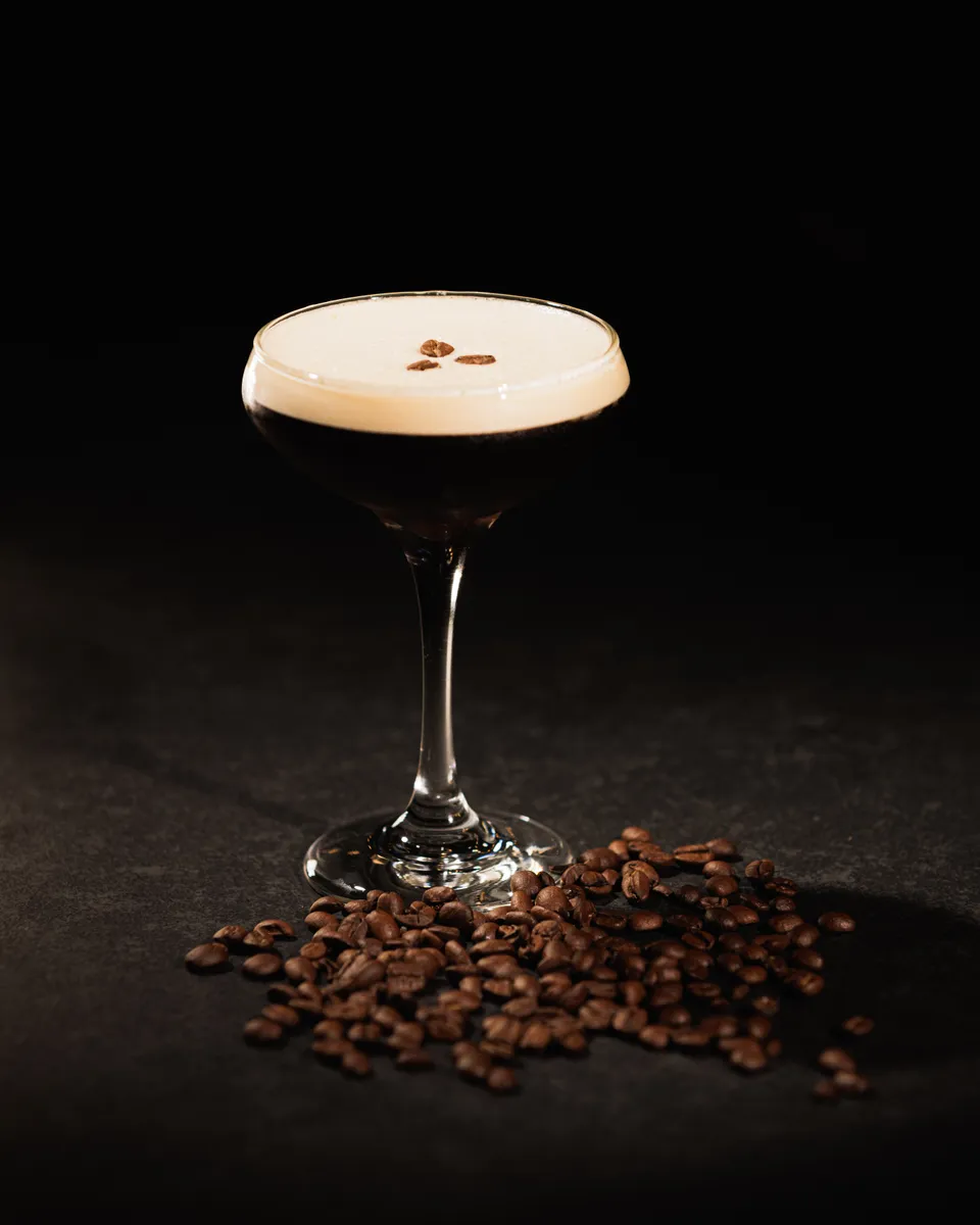 Espresso martini surrounded by scattered coffee beans on black