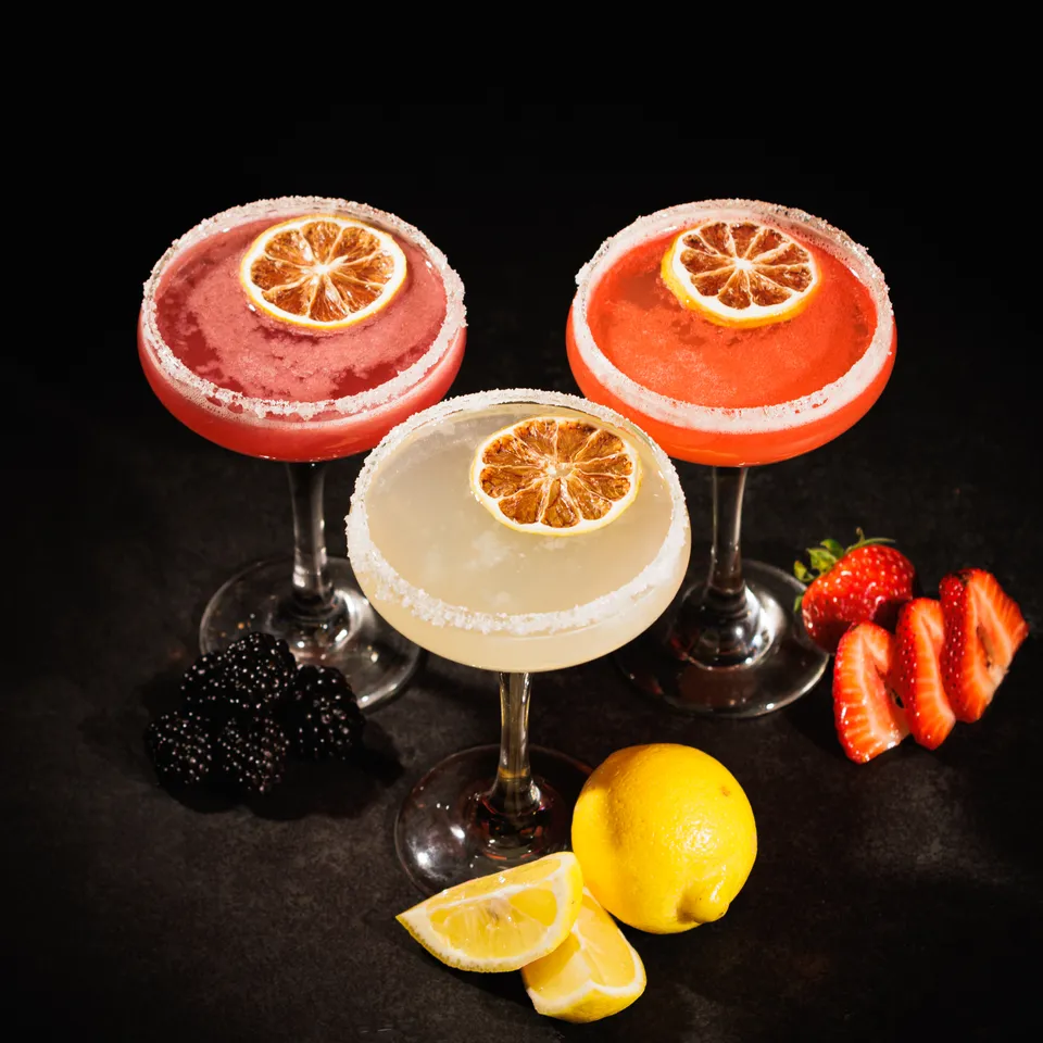 Trio of sugared-rim coupe cocktails garnished with dried citrus and fresh berries