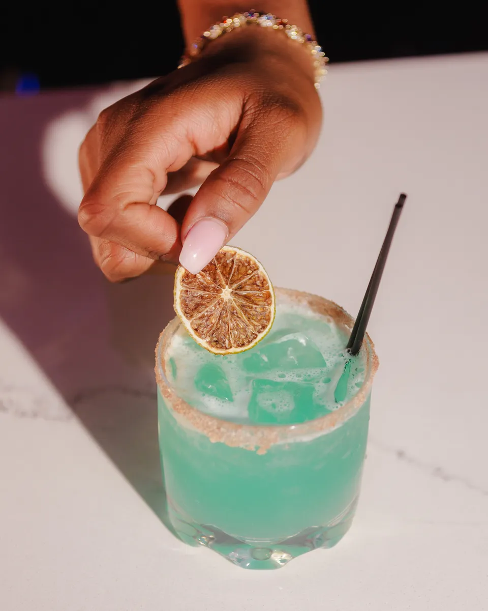 Hand placing a dried lime wheel on a turquoise margarita
